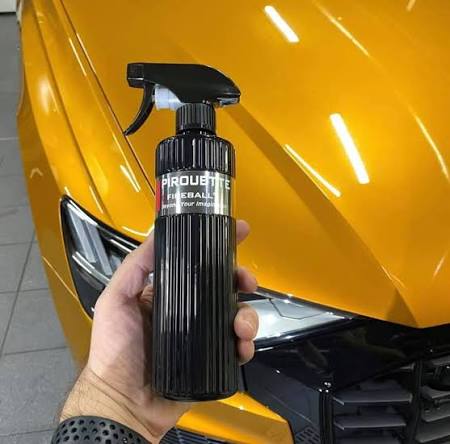 Hand holding a Fireball spray bottle in front of an orange car
