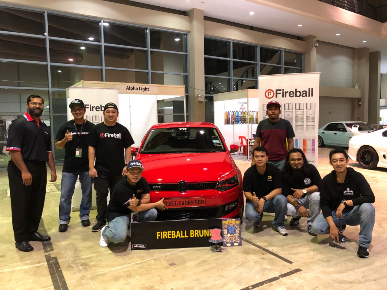 Our Legacy of Excellence in Auto Care Fireball Brunei exhibition group beside a red Volkswagen and Fireball signage at BRIDEX Hall